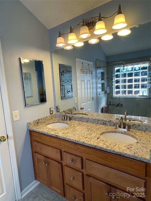 bathroom featuring vaulted ceiling, double vanity, a shower with shower door, and a sink