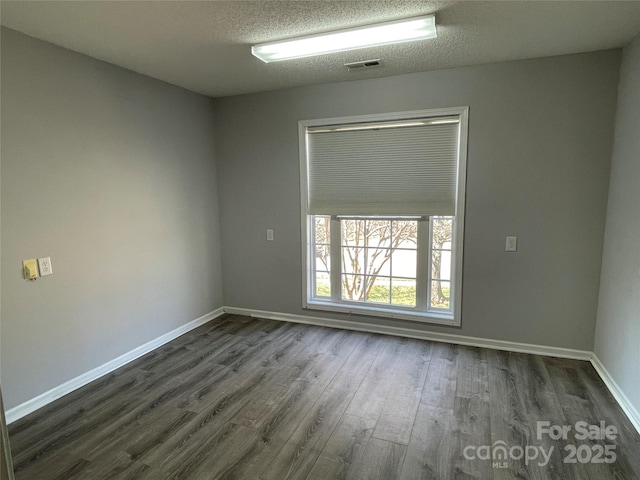 empty room with baseboards, visible vents, dark wood-style flooring, and a textured ceiling