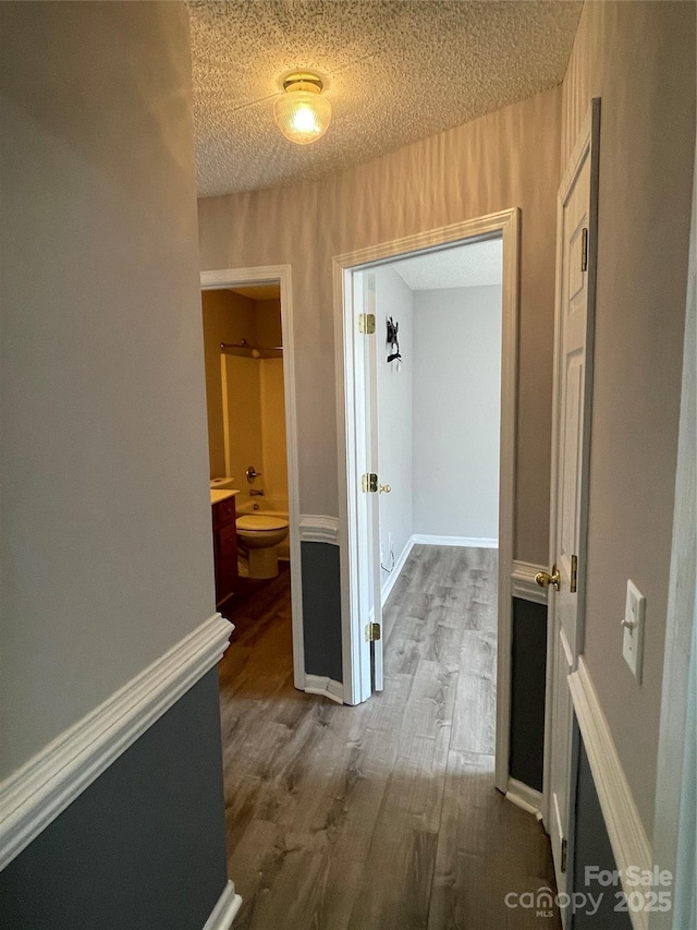 corridor featuring a textured ceiling, dark wood-type flooring, and baseboards