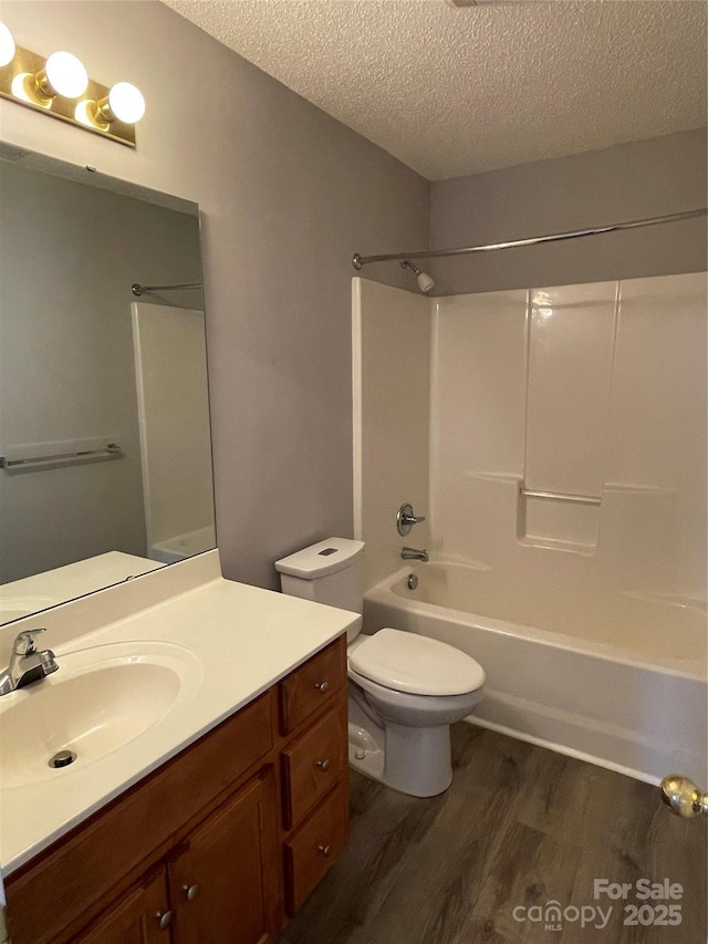 bathroom featuring vanity, wood finished floors, a textured ceiling, bathing tub / shower combination, and toilet