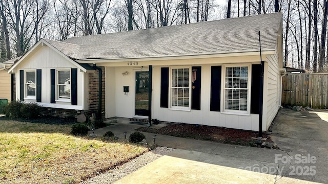 view of front facade featuring fence, brick siding, and a shingled roof