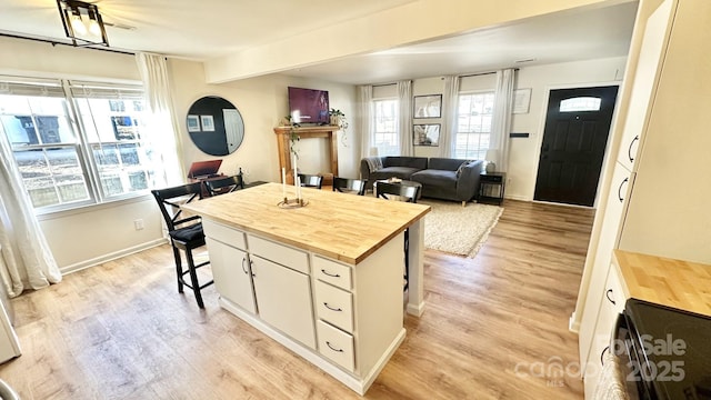 kitchen with baseboards, a breakfast bar, light wood-style flooring, wood counters, and white cabinetry