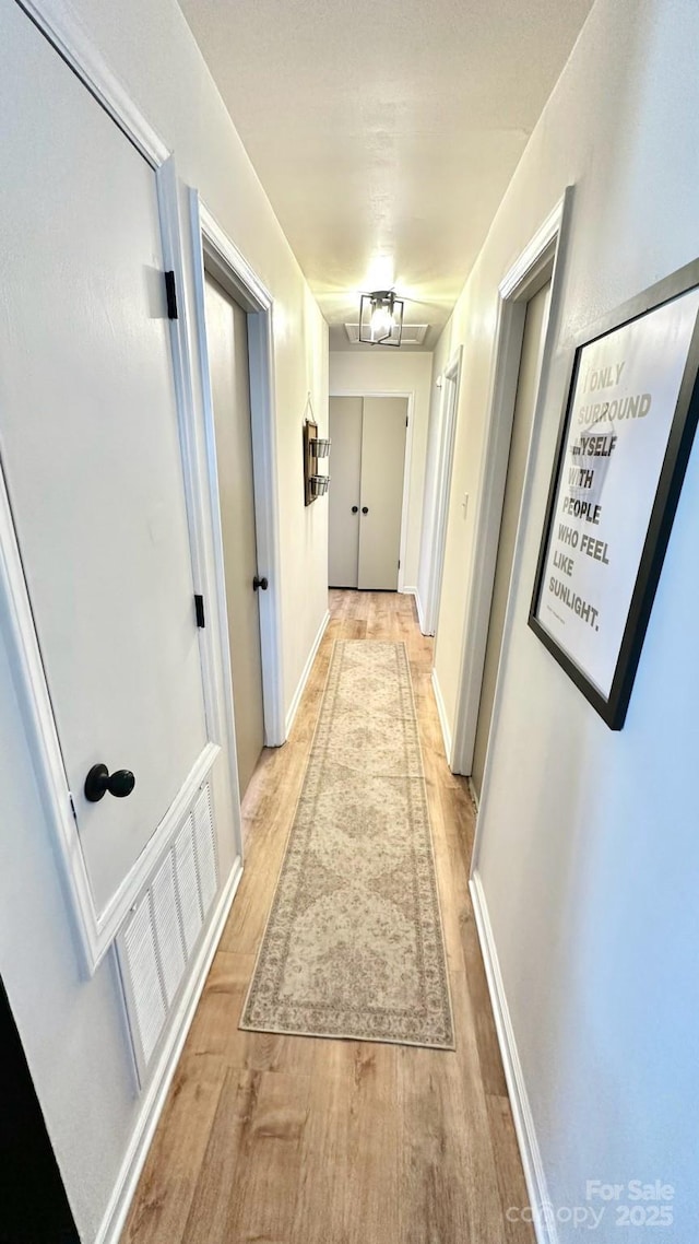 hall featuring visible vents, baseboards, and light wood-style flooring