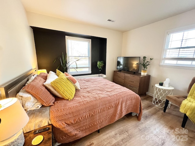 bedroom with visible vents, multiple windows, and wood finished floors