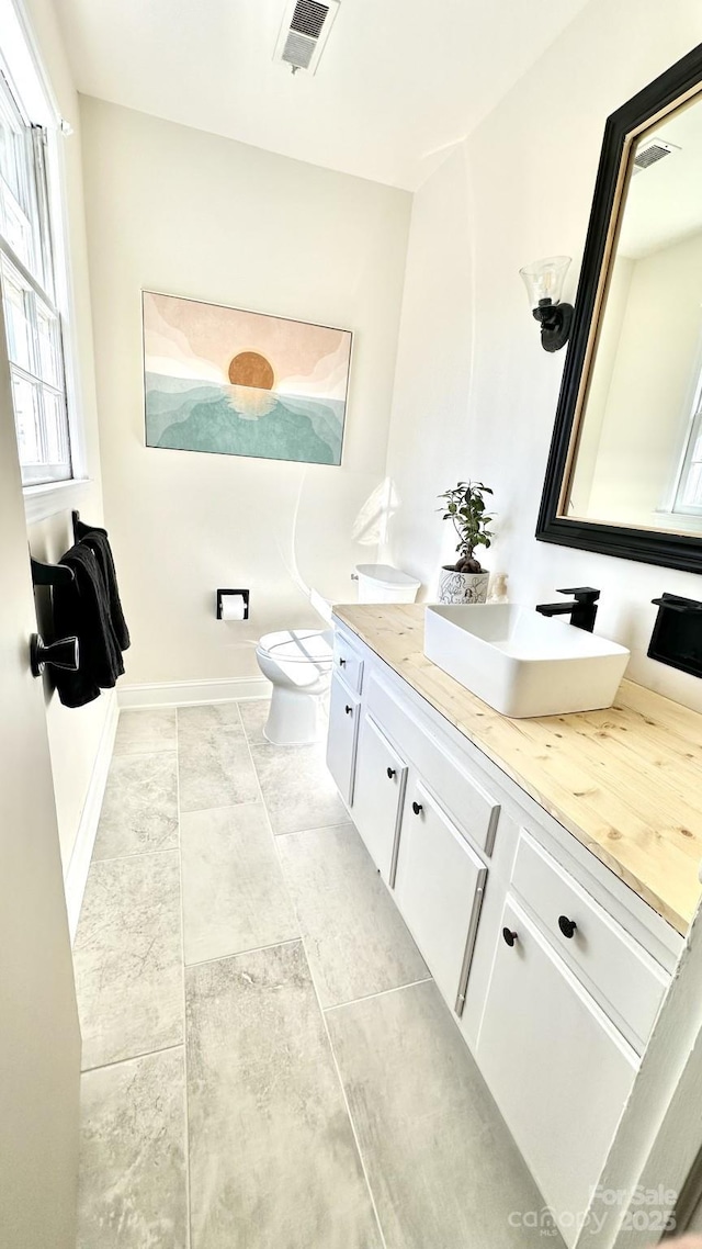 bathroom featuring baseboards, visible vents, double vanity, a sink, and toilet