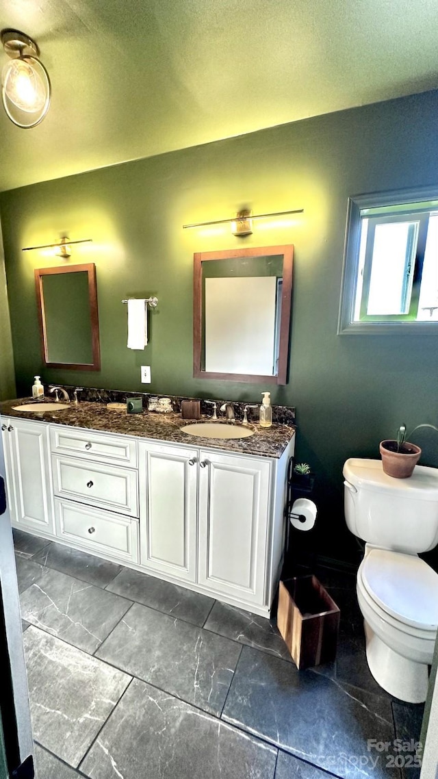 bathroom with double vanity, toilet, and a sink