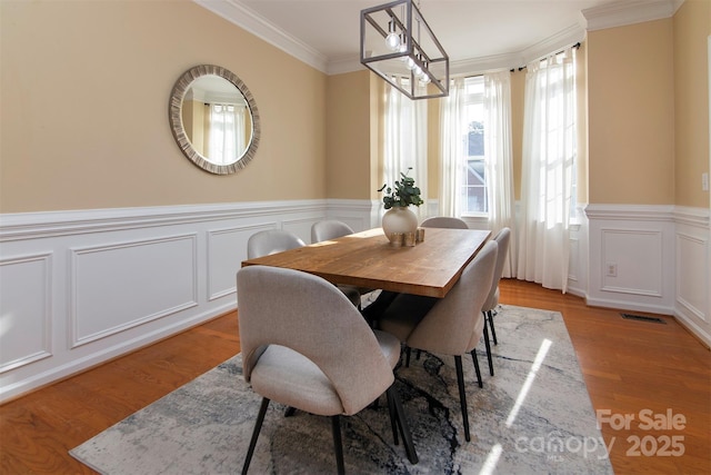 dining room with visible vents, crown molding, light wood-style floors, and a wainscoted wall