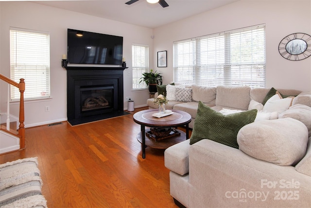 living area with visible vents, a fireplace with flush hearth, a ceiling fan, wood finished floors, and stairs