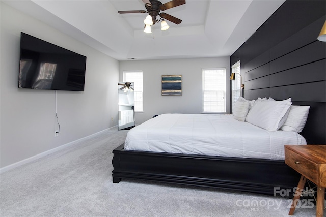 carpeted bedroom with a raised ceiling, baseboards, and ceiling fan