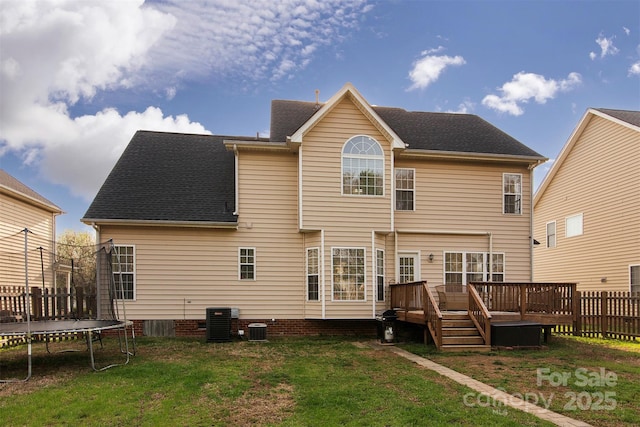 back of property featuring a trampoline, fence, a yard, a wooden deck, and central AC unit