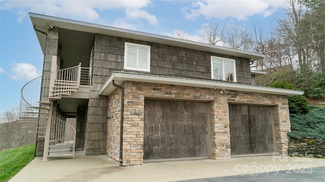 exterior space featuring stairs, an attached garage, stone siding, and driveway