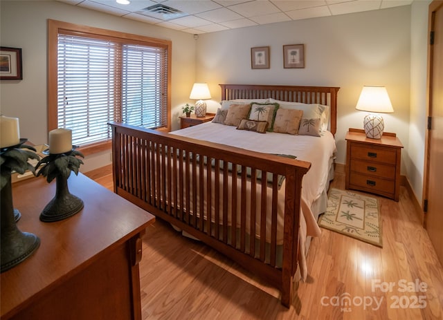 bedroom featuring visible vents, baseboards, light wood-type flooring, and a paneled ceiling