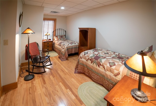 bedroom with wood finished floors, visible vents, a drop ceiling, and baseboards