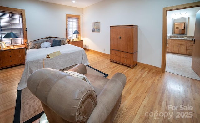 bedroom with baseboards, light wood-type flooring, ensuite bathroom, and a sink