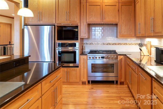 kitchen featuring brown cabinetry, light wood-style flooring, stainless steel appliances, decorative backsplash, and pendant lighting