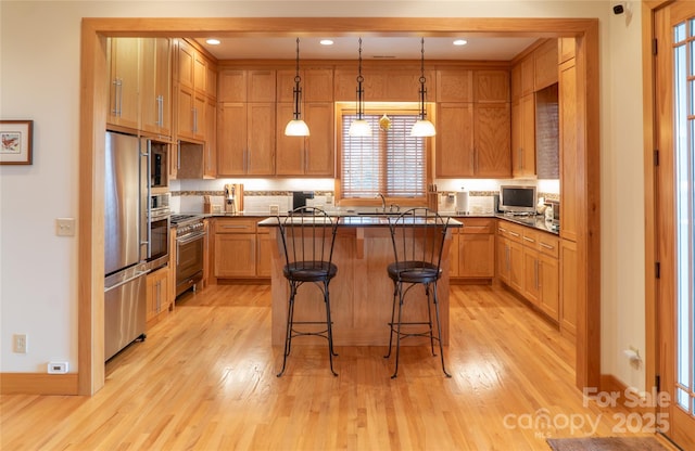 kitchen featuring a kitchen island, pendant lighting, light wood-style flooring, appliances with stainless steel finishes, and a kitchen breakfast bar