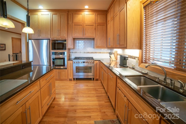 kitchen featuring light wood-style flooring, a sink, appliances with stainless steel finishes, pendant lighting, and backsplash