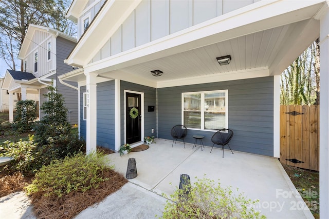 doorway to property with a porch, board and batten siding, and fence