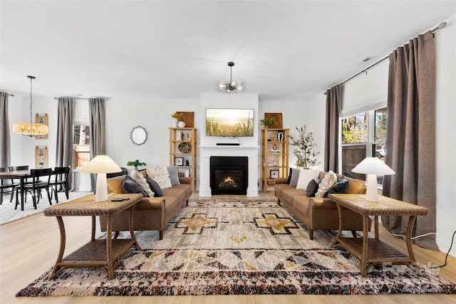 living area with a notable chandelier, a glass covered fireplace, and wood finished floors