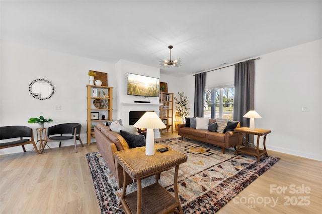 living room with baseboards, an inviting chandelier, a fireplace, and light wood finished floors