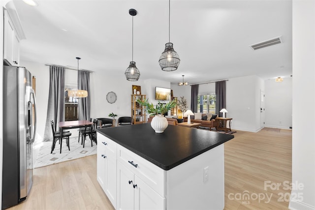 kitchen featuring visible vents, light wood-style flooring, stainless steel refrigerator with ice dispenser, dark countertops, and open floor plan