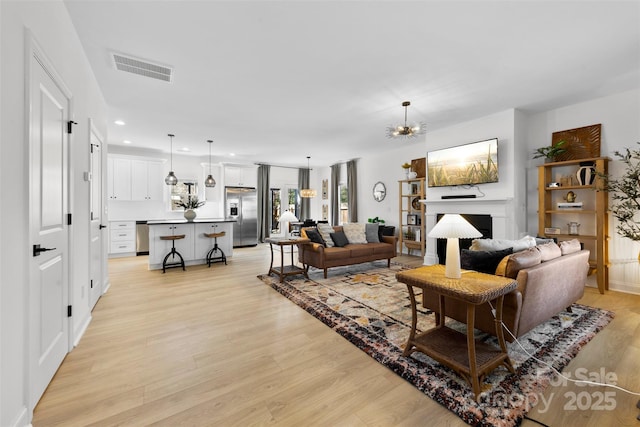 living room featuring recessed lighting, visible vents, a fireplace, and light wood finished floors