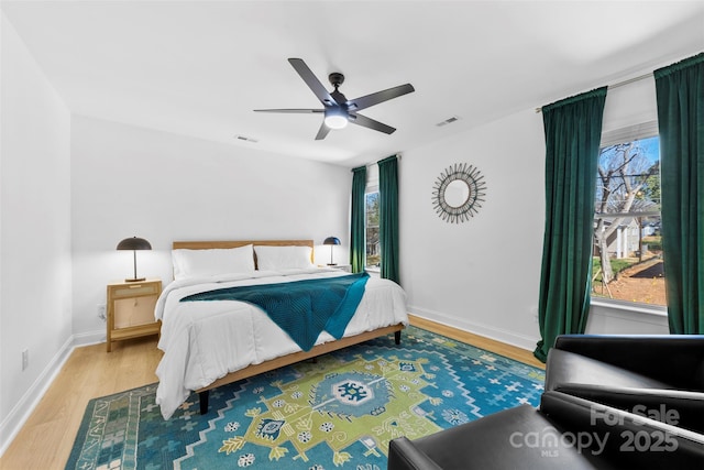 bedroom with ceiling fan, visible vents, baseboards, and wood finished floors