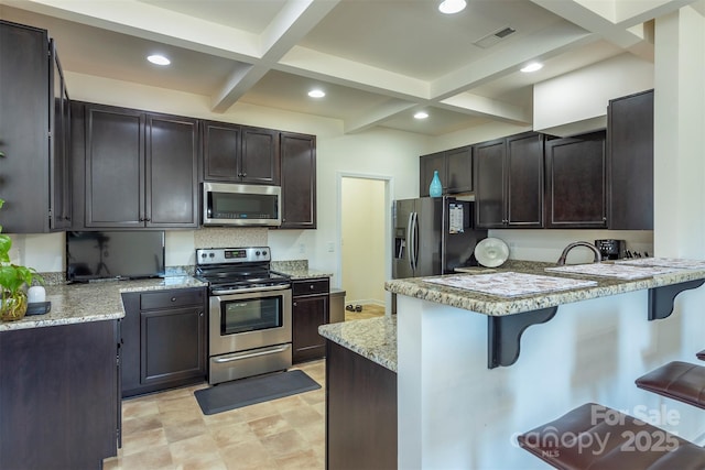 kitchen with beamed ceiling, a peninsula, stainless steel appliances, and a kitchen bar