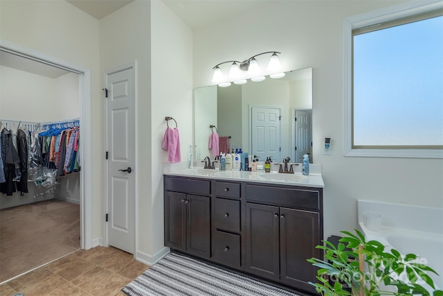 full bathroom featuring double vanity, a walk in closet, a tub to relax in, and a sink