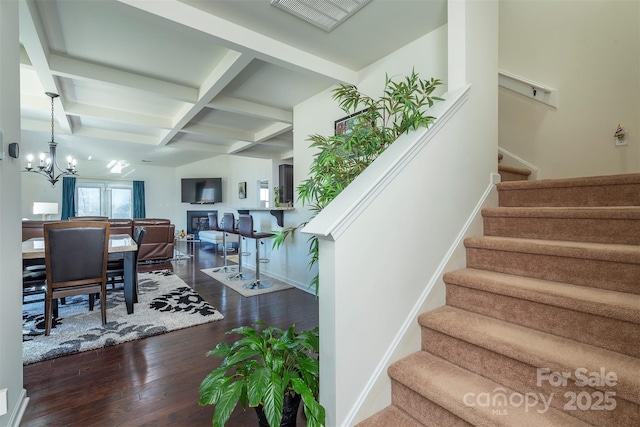 stairway featuring beamed ceiling, coffered ceiling, wood finished floors, an inviting chandelier, and baseboards