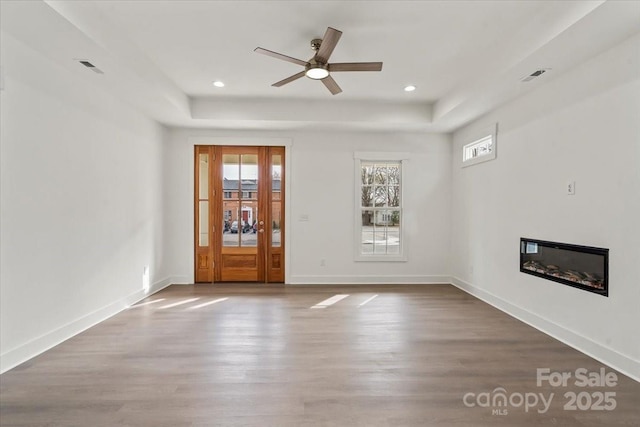 unfurnished living room with a tray ceiling, wood finished floors, and baseboards