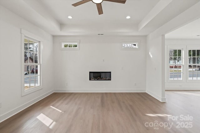 unfurnished living room featuring baseboards, a raised ceiling, and wood finished floors