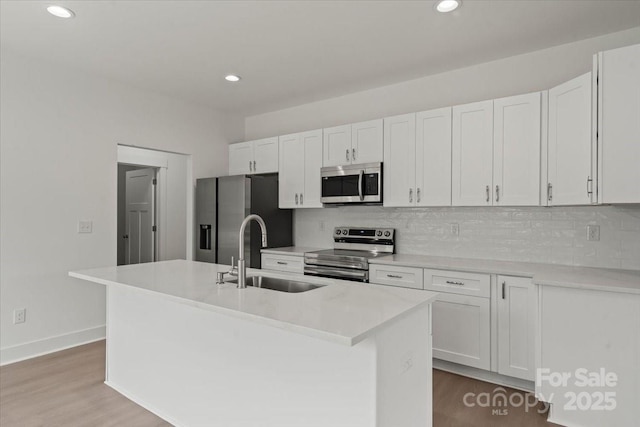 kitchen with a center island with sink, a sink, backsplash, white cabinetry, and appliances with stainless steel finishes