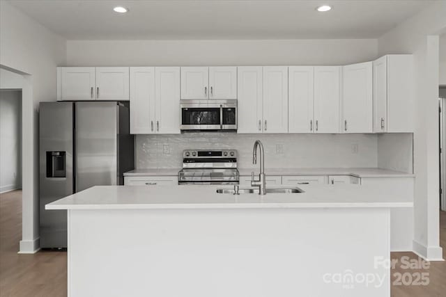 kitchen with a center island with sink, a sink, light countertops, appliances with stainless steel finishes, and white cabinetry