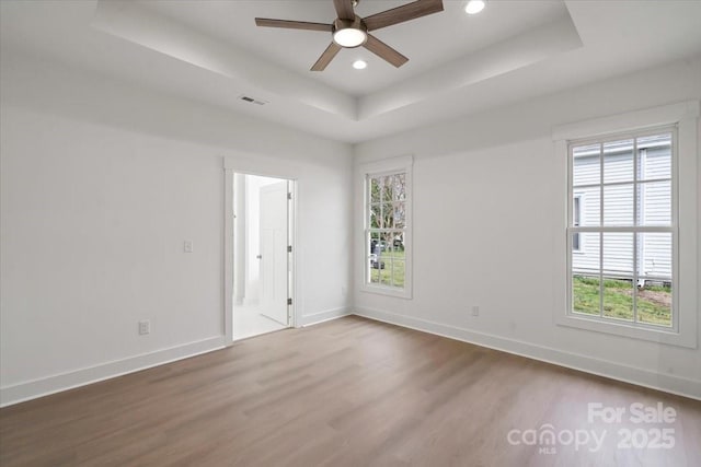 spare room featuring visible vents, ceiling fan, baseboards, a tray ceiling, and wood finished floors