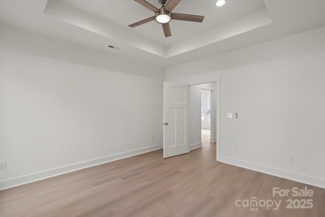 spare room with visible vents, baseboards, a tray ceiling, wood finished floors, and a ceiling fan