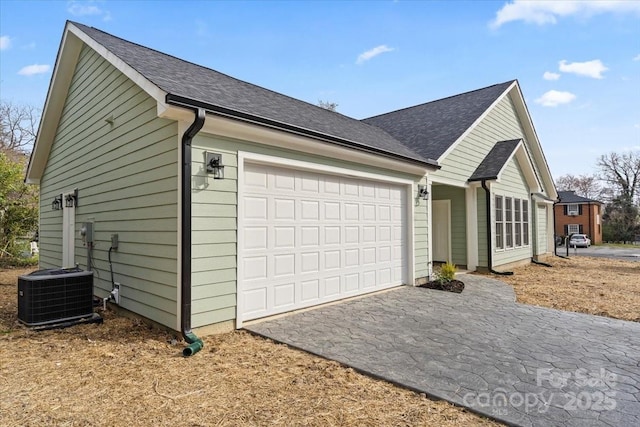 view of side of home with central AC, a garage, driveway, and a shingled roof