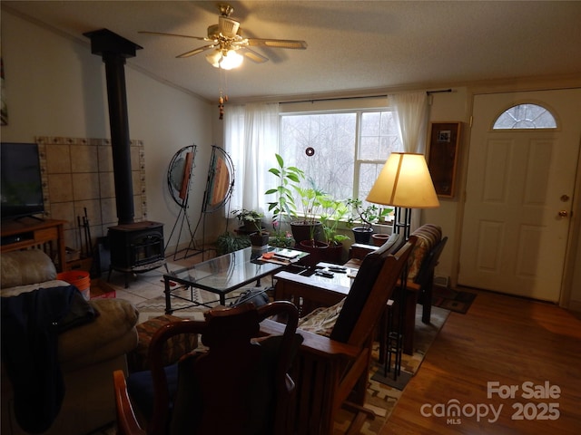 living area featuring wood finished floors, crown molding, ceiling fan, a wood stove, and vaulted ceiling