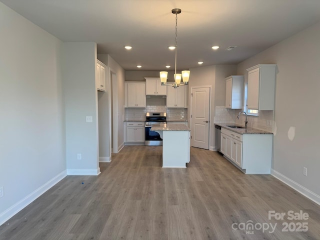 kitchen featuring light wood finished floors, a kitchen island, a sink, white cabinets, and appliances with stainless steel finishes