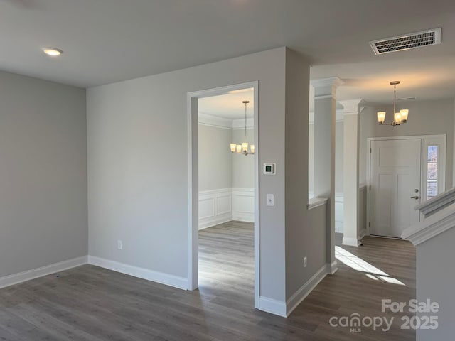 empty room with visible vents, dark wood finished floors, an inviting chandelier, wainscoting, and crown molding