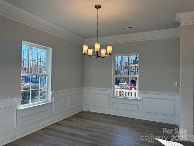 unfurnished dining area featuring visible vents, ornamental molding, dark wood-style floors, an inviting chandelier, and wainscoting