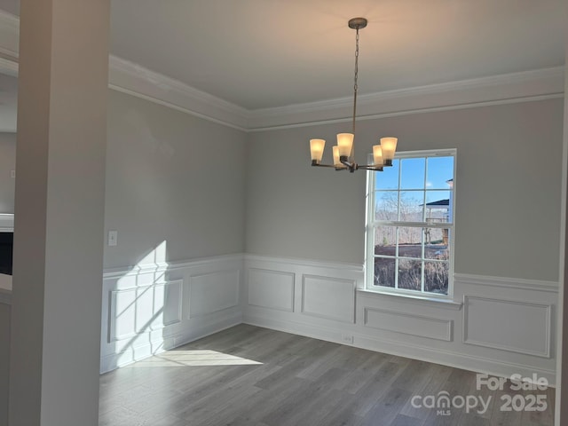 unfurnished dining area featuring a wainscoted wall, crown molding, an inviting chandelier, and wood finished floors