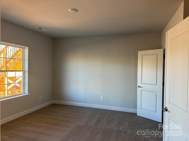 unfurnished room with visible vents, baseboards, and dark carpet