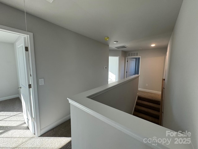 hall with an upstairs landing, visible vents, dark carpet, and baseboards