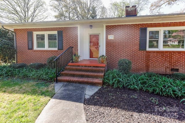 view of exterior entry with brick siding, crawl space, and a chimney