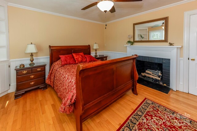 bedroom featuring a fireplace with flush hearth, crown molding, and a wainscoted wall