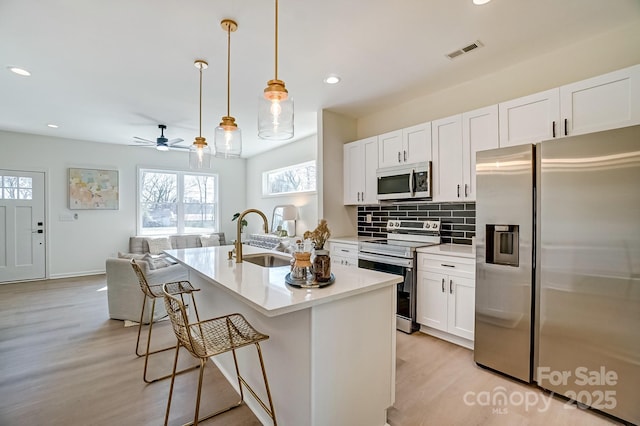 kitchen featuring visible vents, a breakfast bar, a sink, tasteful backsplash, and stainless steel appliances