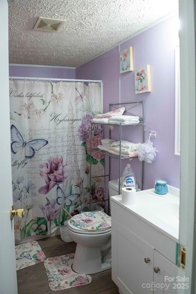 bathroom with visible vents, toilet, vanity, wood finished floors, and a textured ceiling