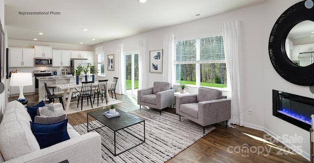 living room featuring dark wood-style floors, a glass covered fireplace, recessed lighting, and baseboards