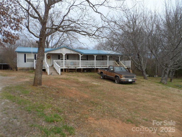 view of front of home featuring covered porch, driveway, metal roof, and a front lawn